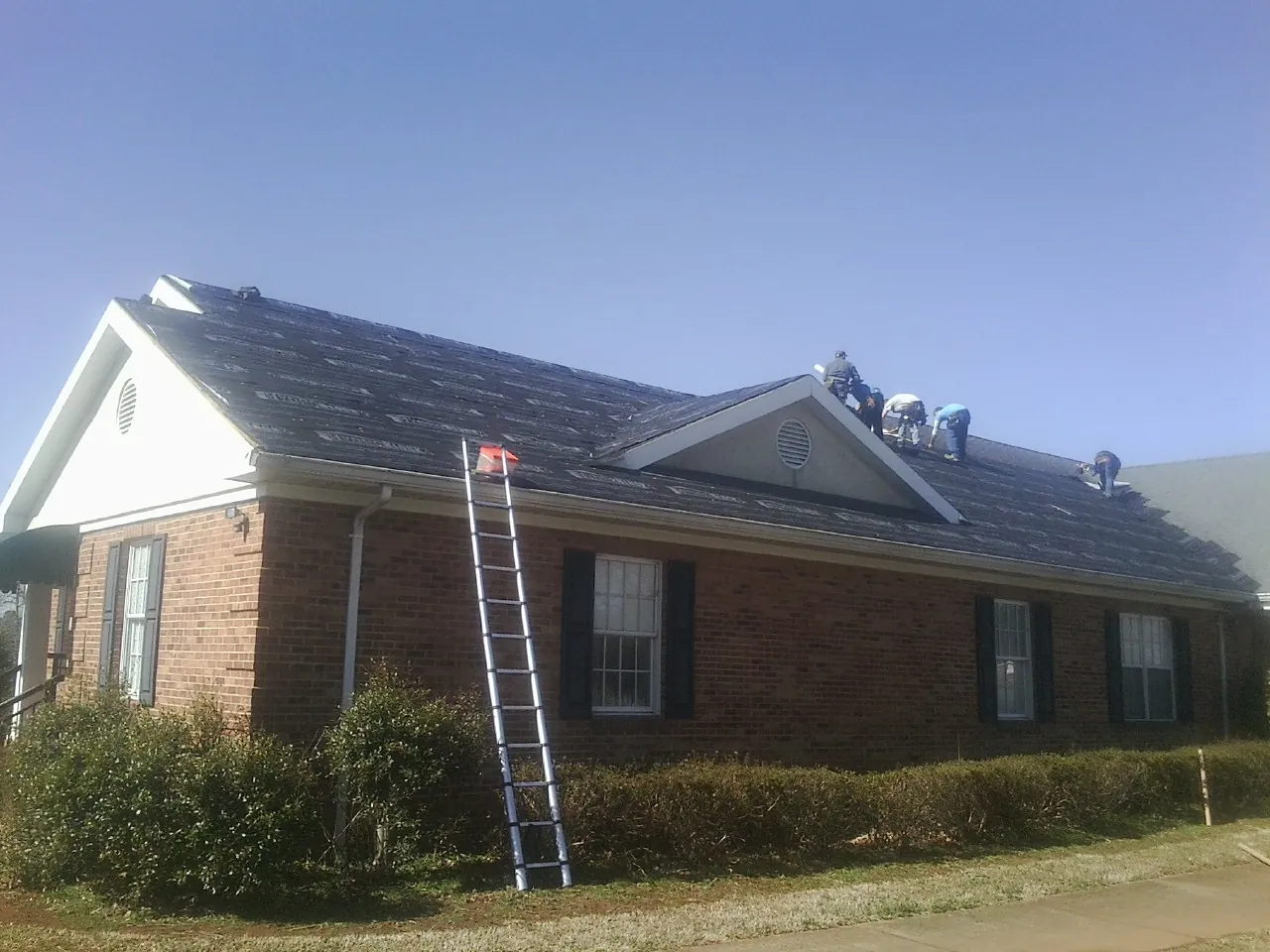 Crew tearing shingles off a brick ranch roof with a ladder set — Emergency Roof Repair work by our crew in Yarmouth Port