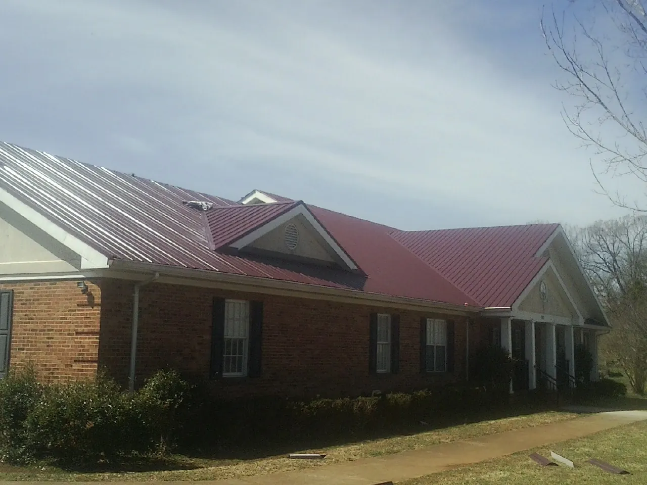 Red metal roof with gabled entries on a long brick building, from a Hail Damage Roof Repair job in Yarmouth Port