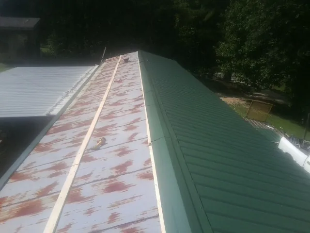 Old rusted panels beside newly installed green metal roofing in Yarmouth Port