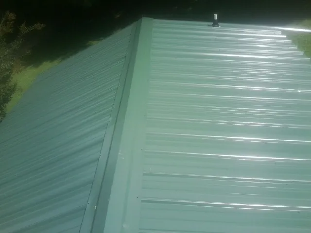New green metal panels meeting at the ridge of a roof — Flat Roof Repair work by our crew in Yarmouth Port
