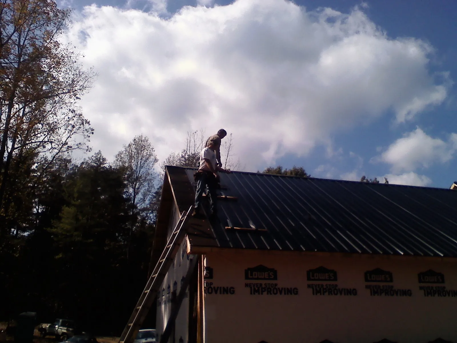 Roofer fastening dark metal panels high against a cloudy sky, from a Roof Inspection job in Yarmouth Port