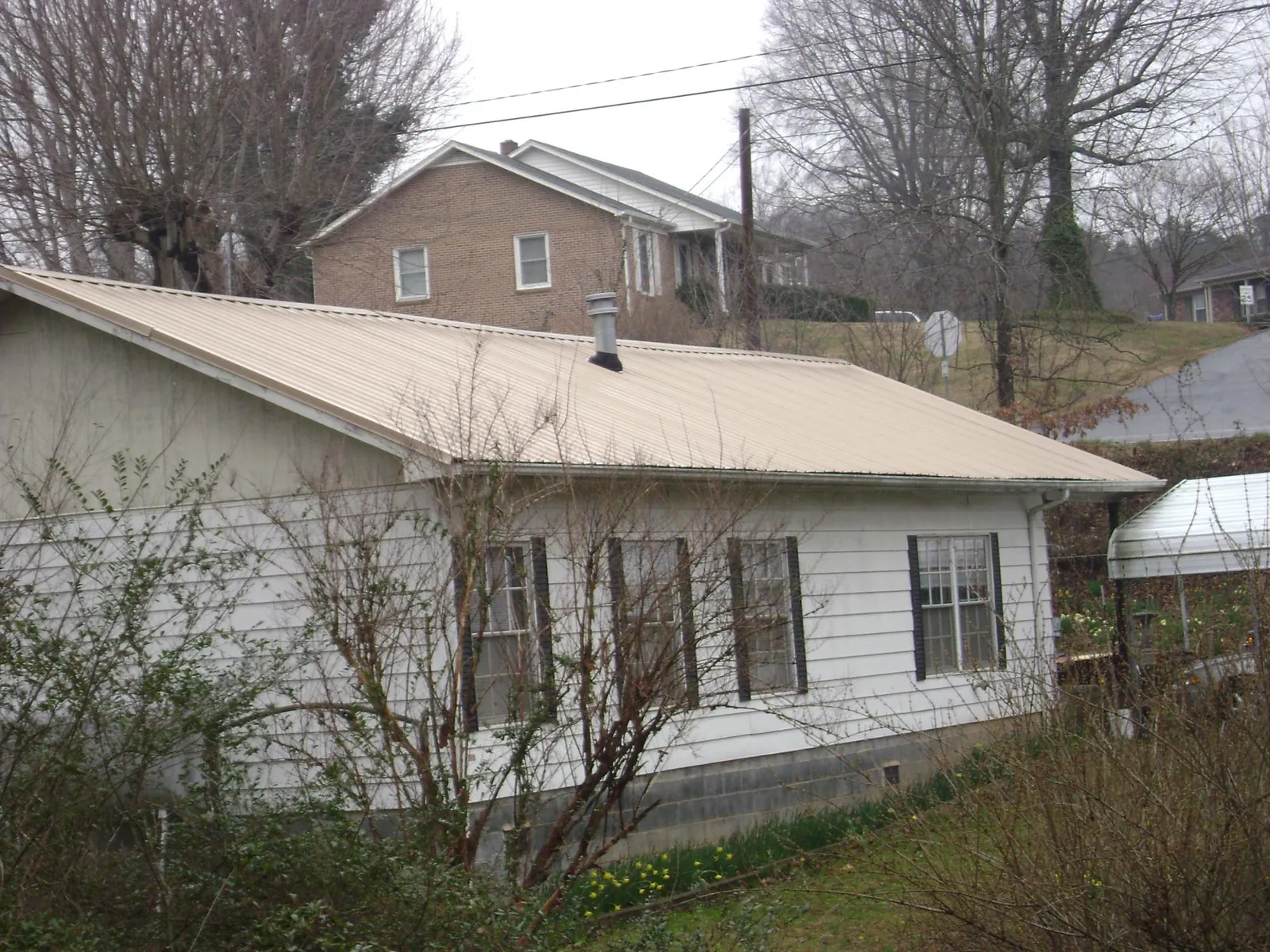 Tan metal roof on a white sided house set into a hillside — Commercial Roofing by Roofing Brothers in Yarmouth Port